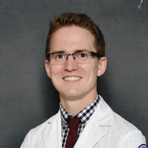 Smiling person in white coat with glasses.