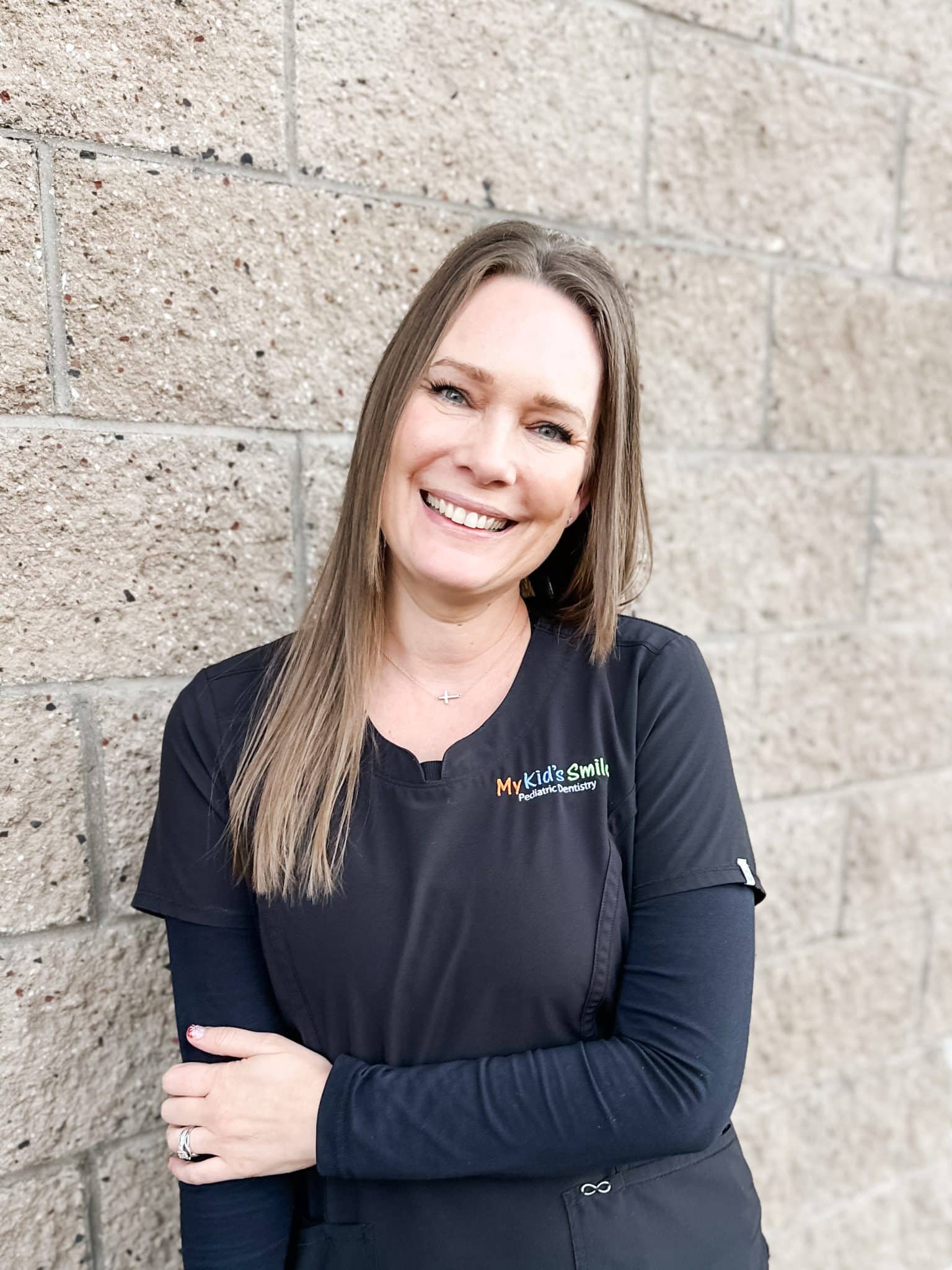 Smiling woman in dental uniform against brick wall.