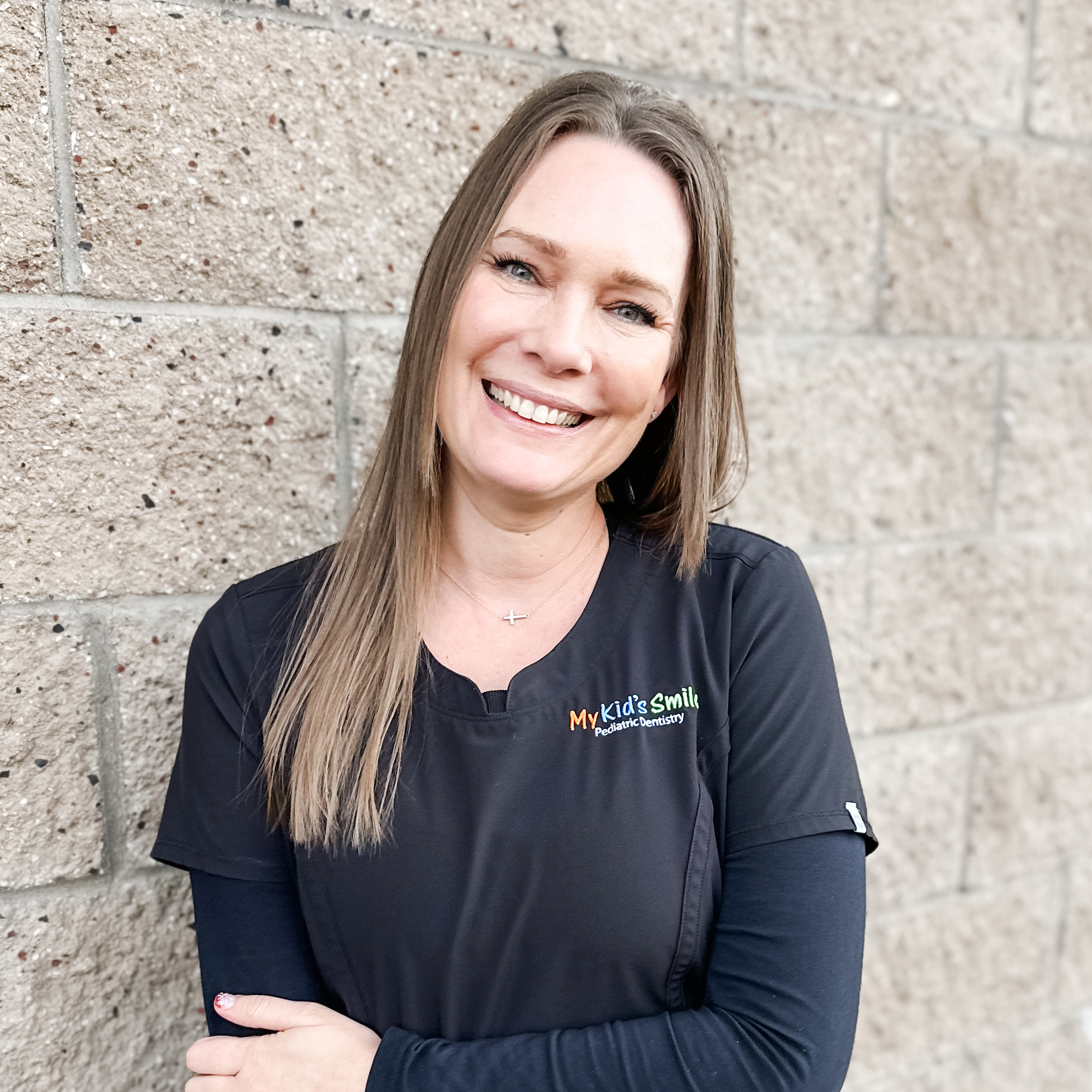 Smiling person in pediatric dentistry uniform outside wall