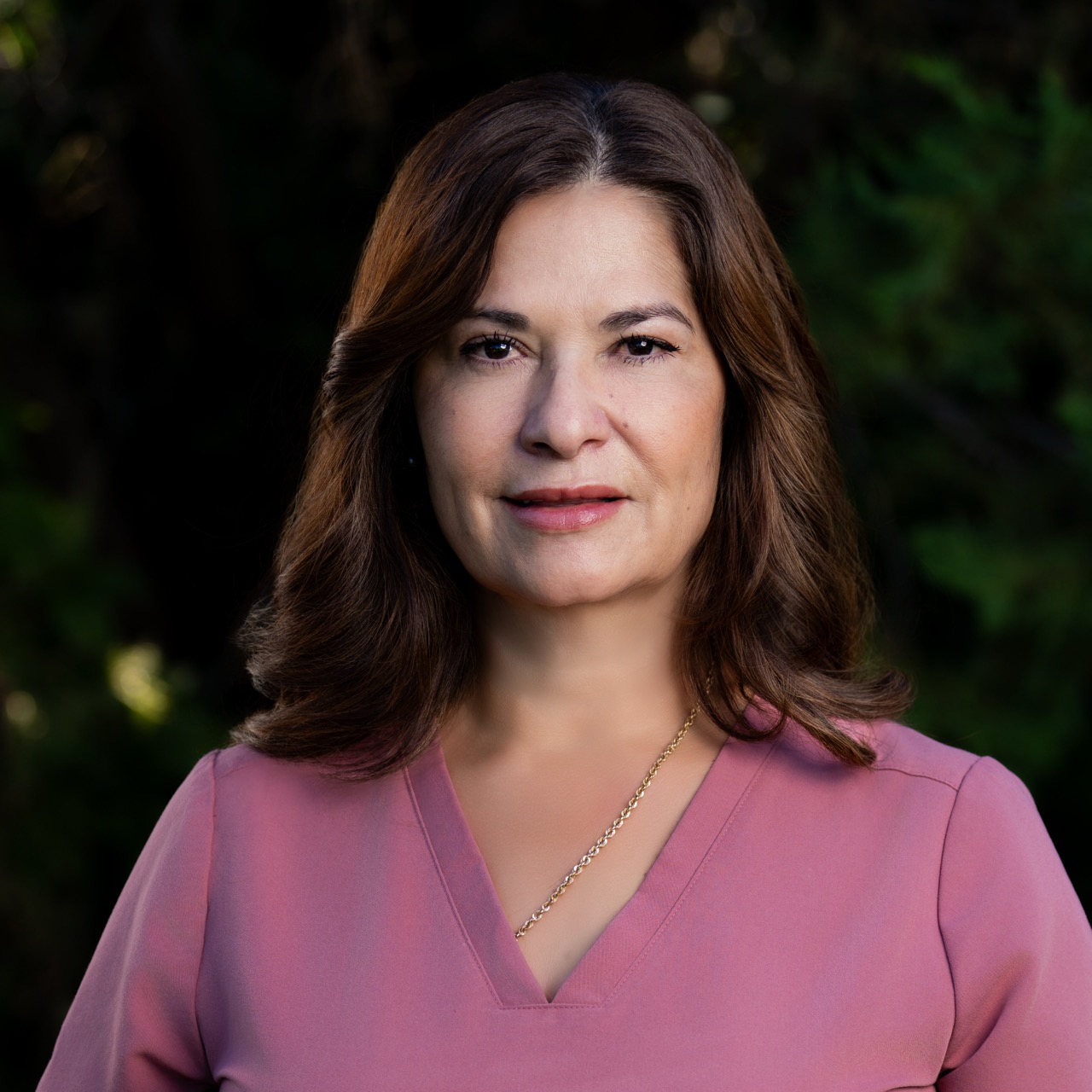 Woman smiling outdoors in pink top.