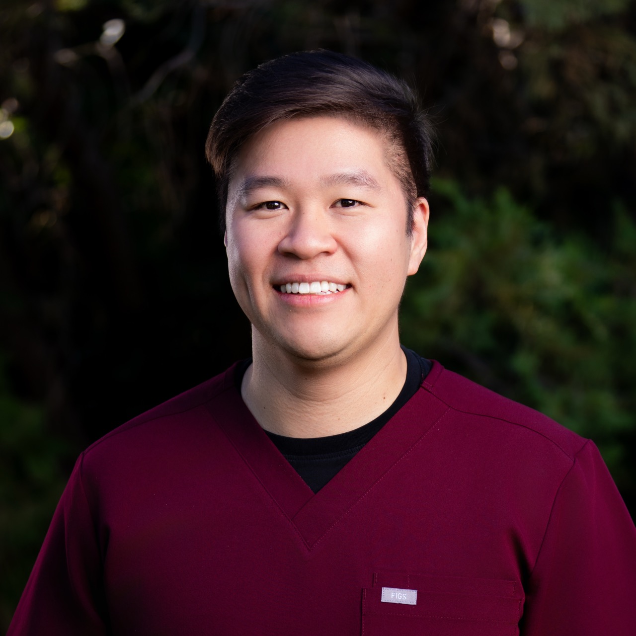 Person smiling outdoors in burgundy scrubs.