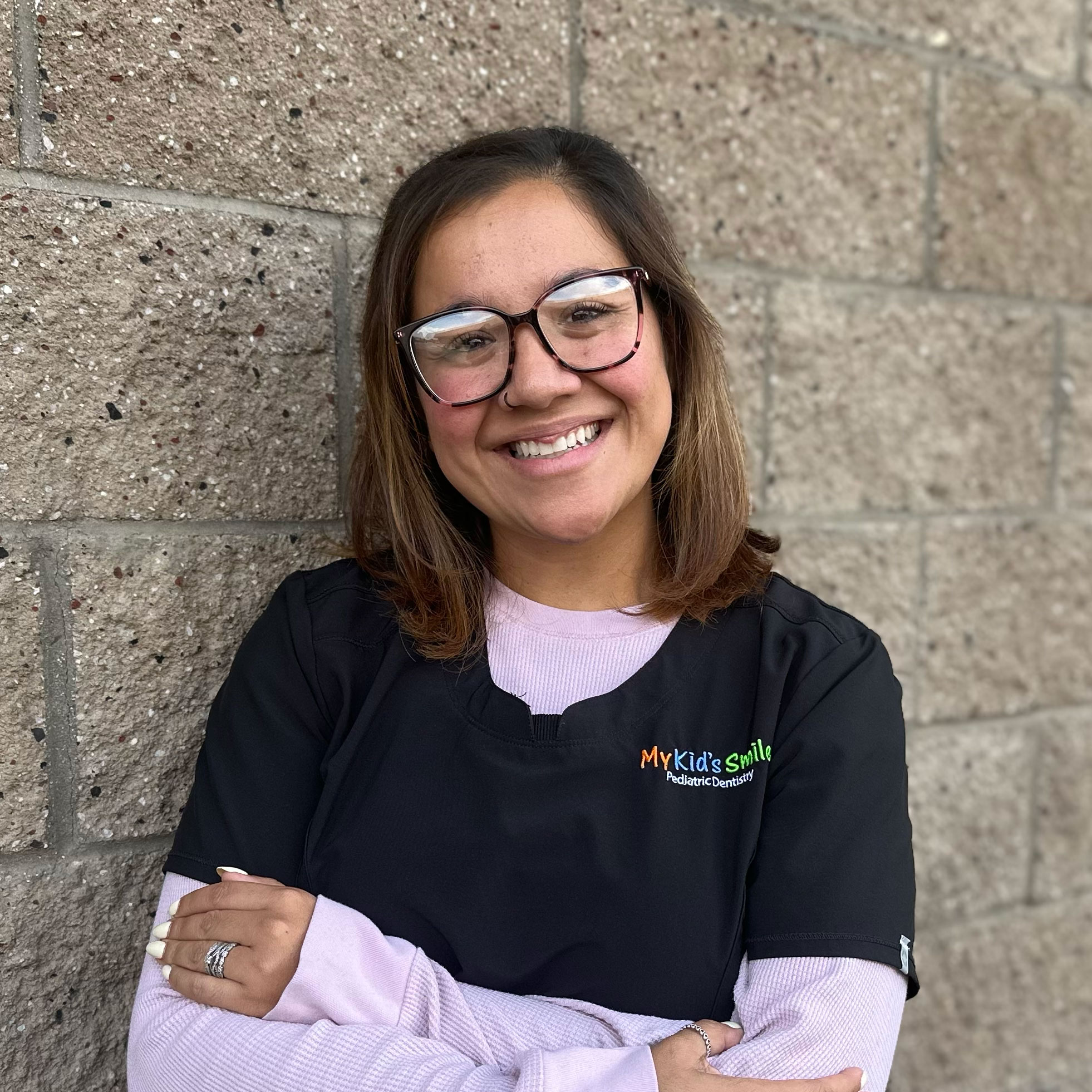 Smiling woman in dental attire against brick wall.